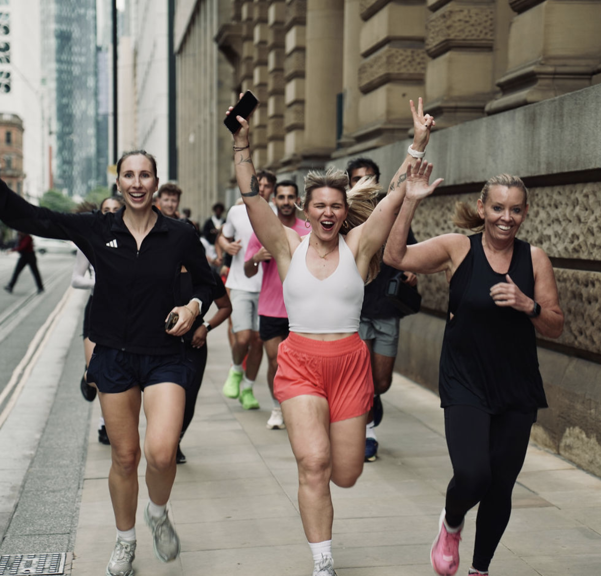 Line sprinting down a city street with two running club friends, arms raised