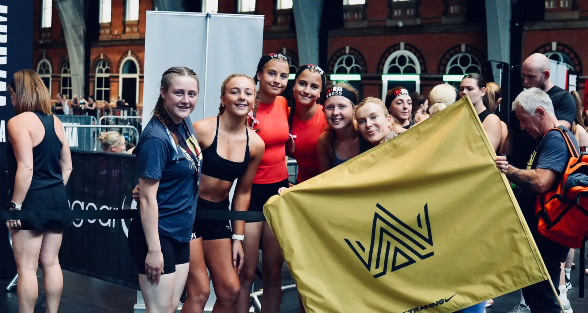 Line and fellow athletes huddled together holding a yellow Rox Queens flag at an indoor race